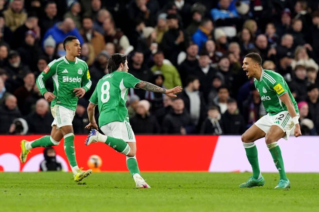 Newcastle United Football Club player Sandro Tonali celebrates scoring a goal, running away to be congratulated by two teammates while raising an arm on a green grass pitch. All three players are wearing green shirts and socks with white shorts and white lettering on their kits