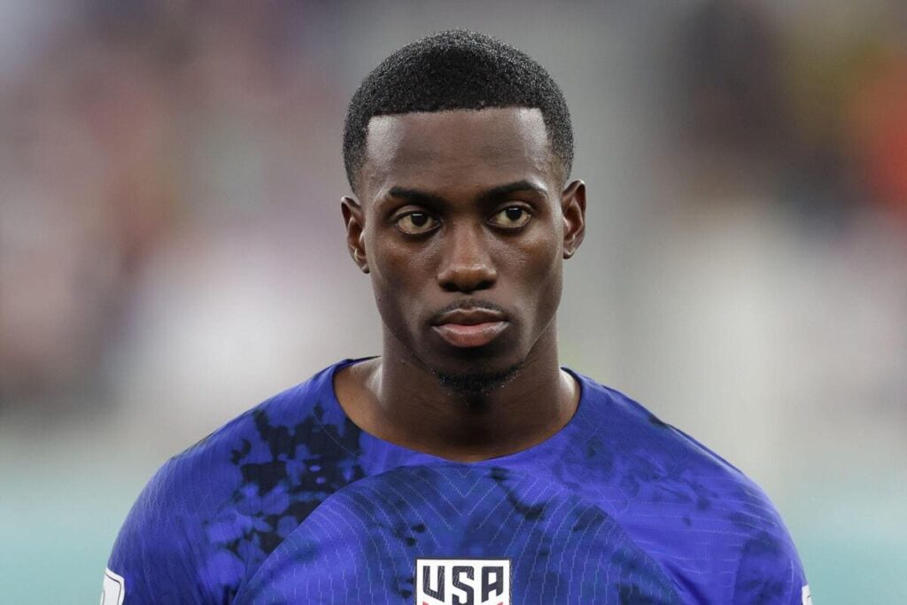 USA international footballer Timothy Weah playing football for the United States of America, standing in a stadium wearing a blue football shirt with black details and the letters USA visible on the front