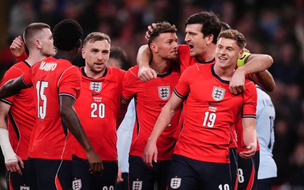 Ben White celebrates a goal for the England national football team while being embraced by his teammates in red shirts