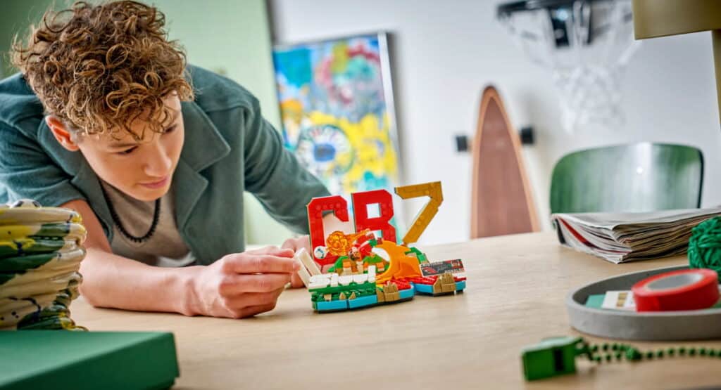 A young designer working on a Lego toy at a table. The designer is wearing a dark top and touching the toy with one hand