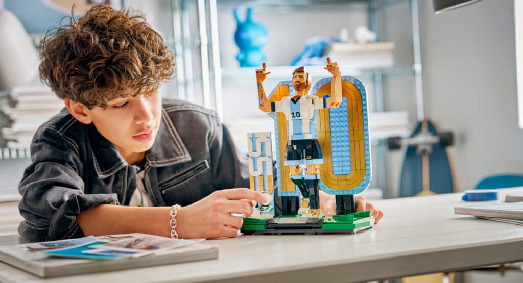 A young designer working on a Lego toy at a table. The designer is wearing a dark top and touching the toy with one hand