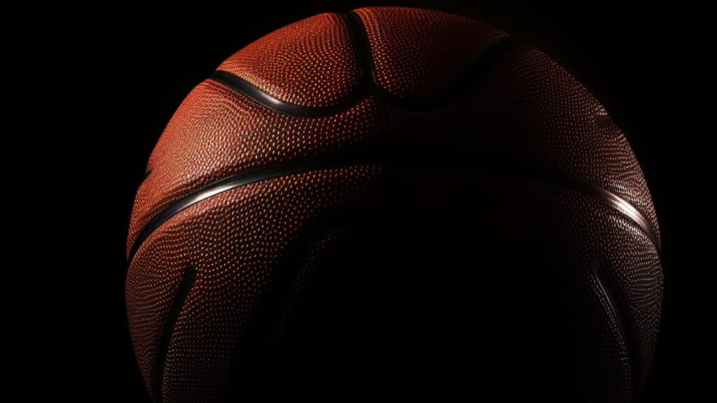 A close up of an NBA basketball in shadows. The ball is dark orange with black lines